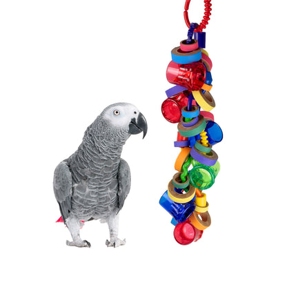 A colorful bird toy consisting of a series of compressed paper rings strung together, with a grey parrot standing next to it.