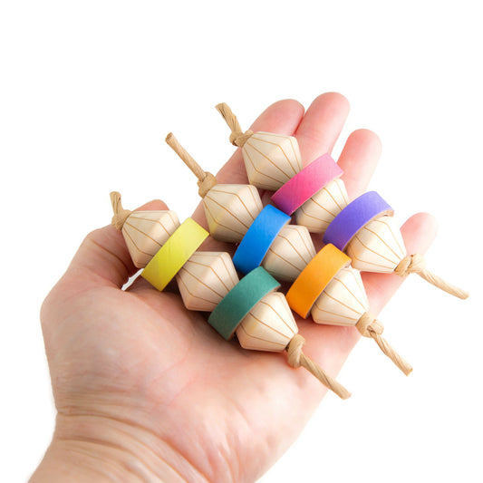Hand holding 3 wooden foot toys for parrots. Engraved diamond shaped beads with birdie bagels in between.